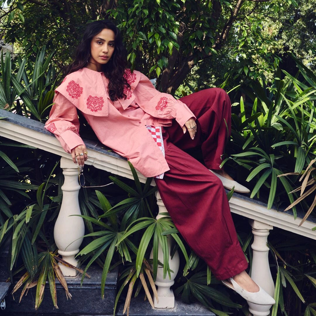 Woman in pink floral outfit sitting on a stone bench with greenery around