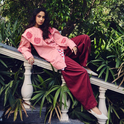 Woman in pink floral outfit sitting on a stone bench with greenery around