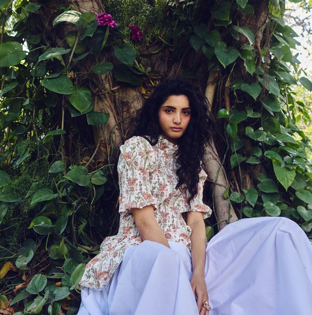 Woman in a floral dress sitting among green foliage