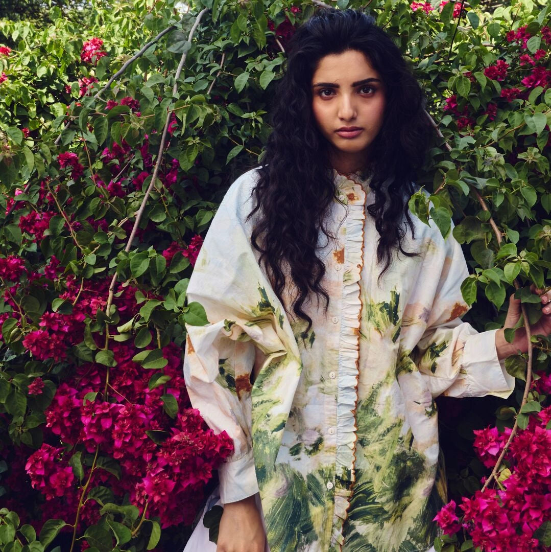 Woman in a floral dress standing among pink flowers and green foliage