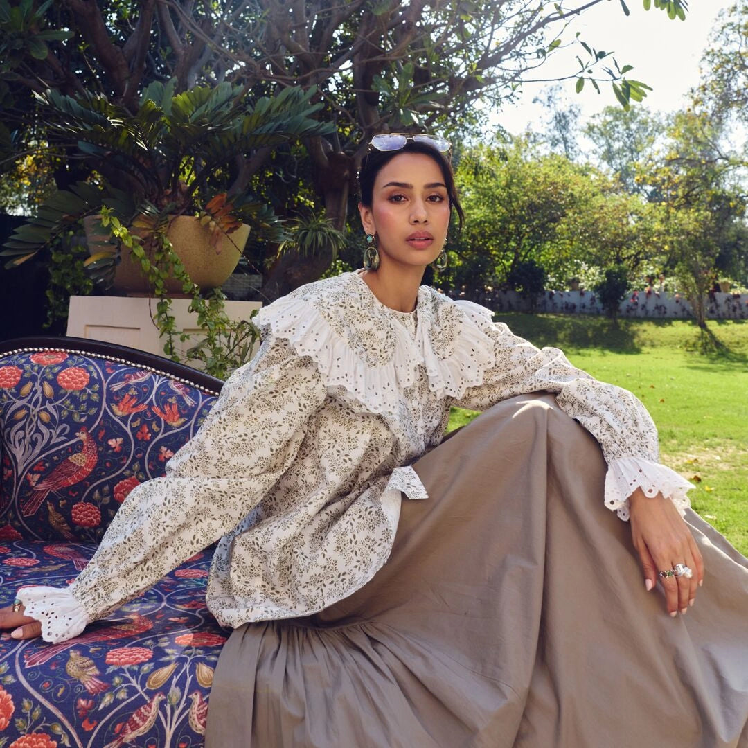 Woman in a patterned outfit sitting outdoors with greenery in the background