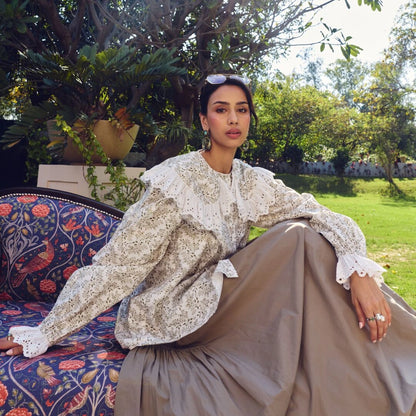 Woman in a patterned outfit sitting outdoors with greenery in the background