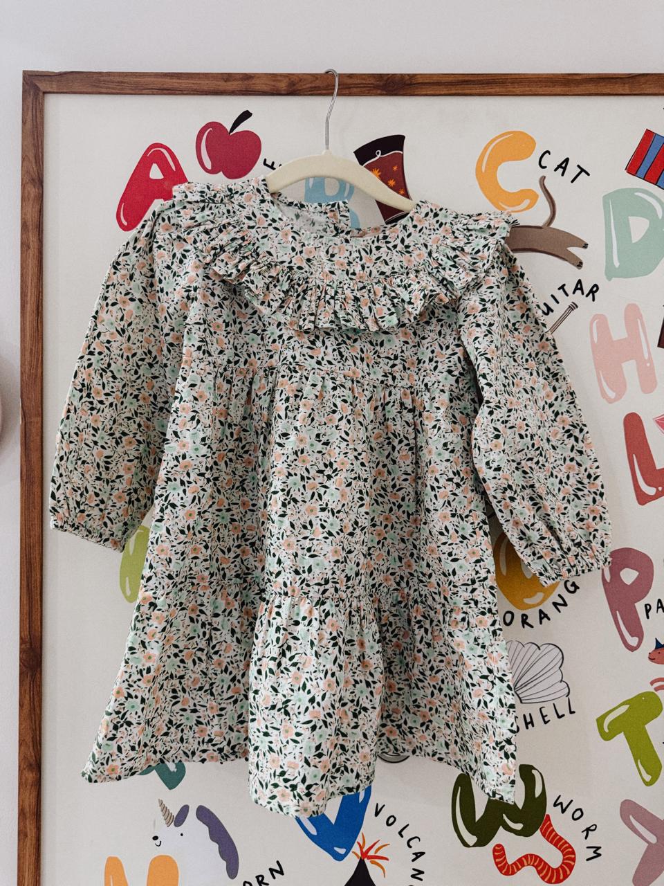 Floral dress hanging on a hanger against a colorful wall with letters and shapes.