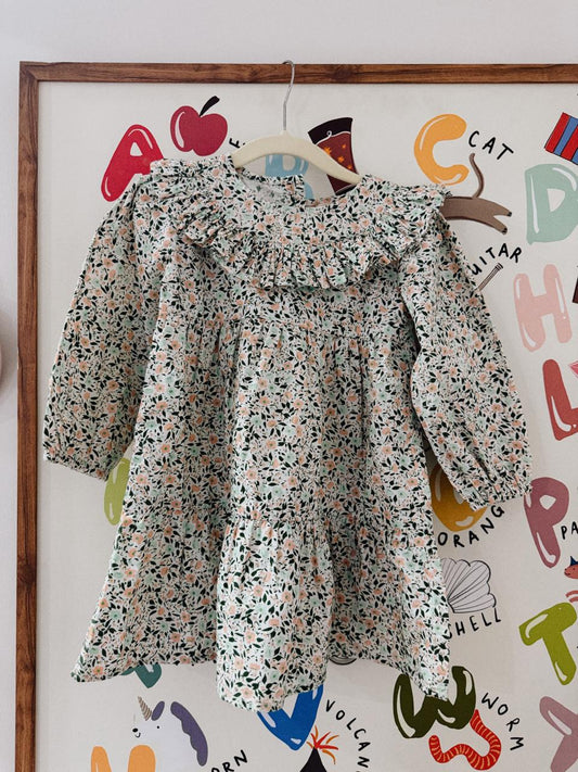 Floral dress hanging on a hanger against a colorful wall with letters and shapes.