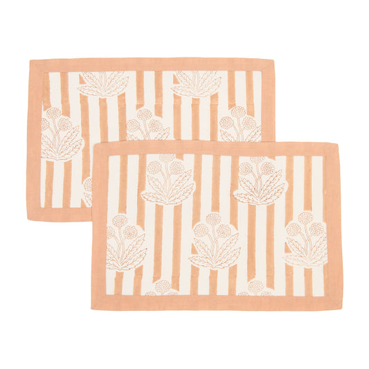 Two peach-colored placemats with white floral patterns on a white background