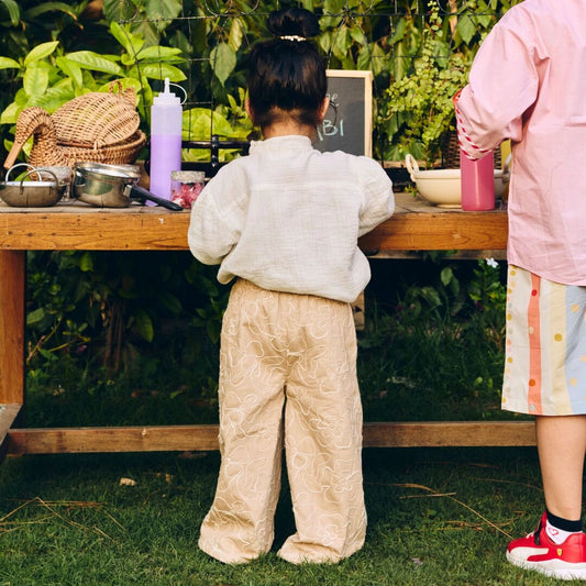 Two children standing at a wooden table outdoors with various items on it.