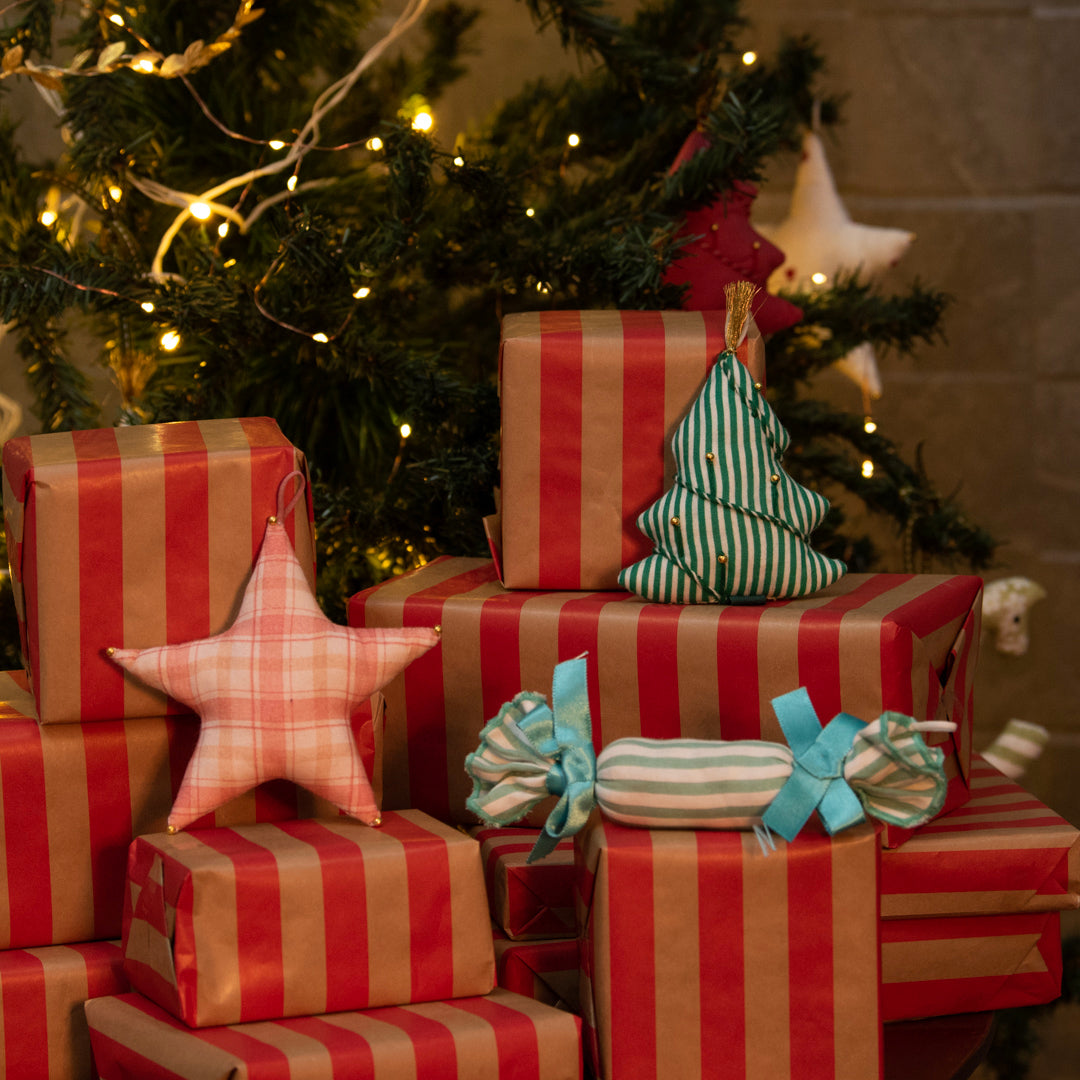 Stack of red and gold striped presents with decorative items in front of a Christmas tree.
