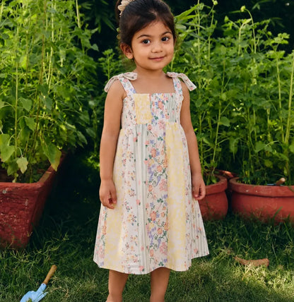 A young girl  wearing a sleeveless midi dress with a soft pastel floral print and tie-shoulder straps.