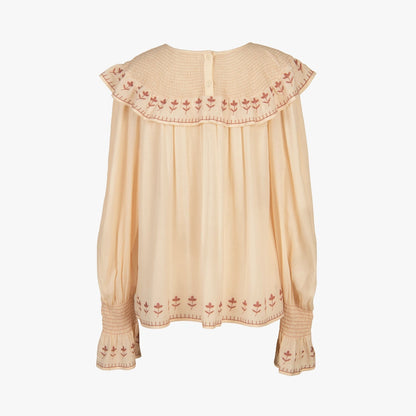 A light beige long-sleeve blouse with a wide pleated ruffled collar and matching ruffled cuffs, featuring delicate red floral embroidery along the edges.