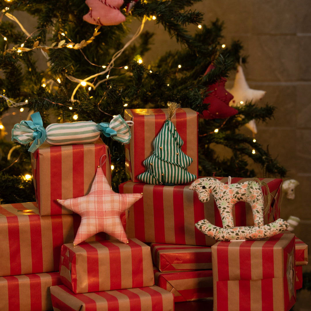 Stack of red and gold striped presents with decorative items under a Christmas tree.