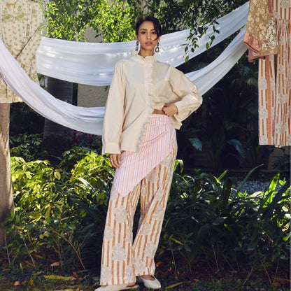 A woman wearing a cream long-sleeve shirt with ruffles and pink-and-white striped pants with lace details.