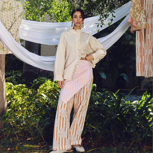 A woman wearing a cream long-sleeve shirt with ruffles and pink-and-white striped pants with lace details.