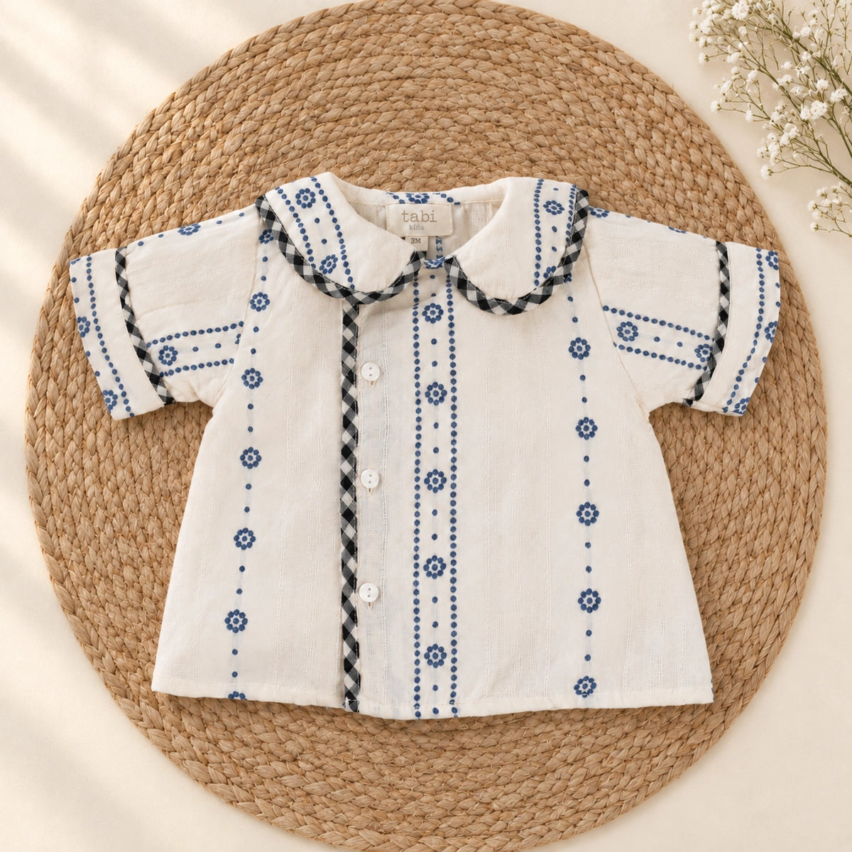 A baby clothing set  featuring a short-sleeve cream shirt with blue embroidered patterns 