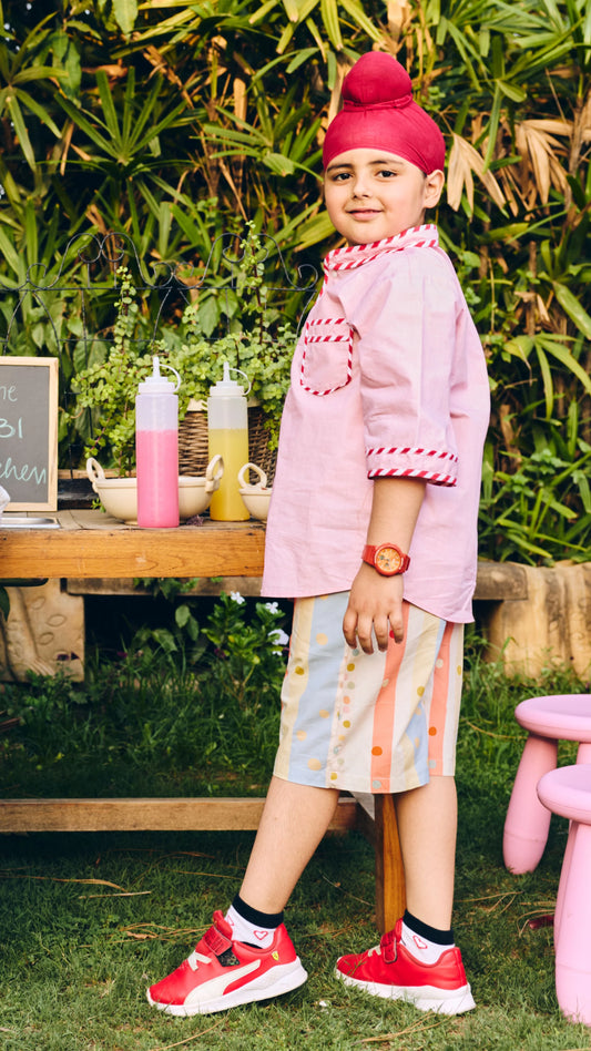 Child in pink outfit with red shoes standing outdoors near a wooden table with bottles.